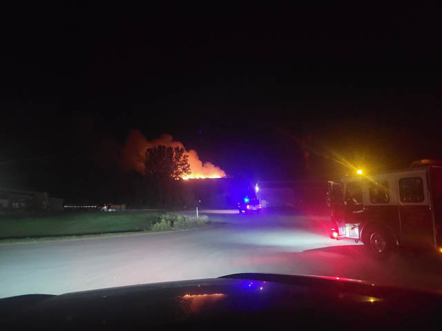 A photo of fire in the distance ahead of a paved road. A fire truck is off to the right near the camera.