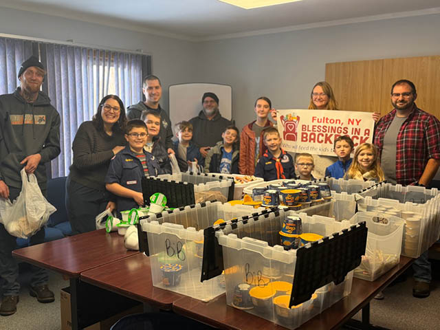 A group of adults and kids standing around a table packed with plastic bins and groceries