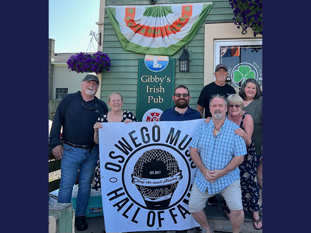 The Board Members of the Oswego Music Hall of Fame and Gibby Thompson, proprietor of Gibby’s Irish Pub come together to promote the upcoming chicken BBQ fundraiser on August 17th. Front row, from left: Bill “Fuzzy” Wiltsie, Carol Dillabough, Norman Berlin, Ron Castaldo, Gibby Thompson Sonia Lough-Berlin and Nancy Spereno. 