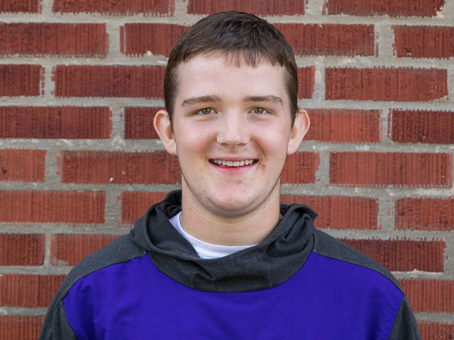 A young white male-presenting student in front of a brick wall