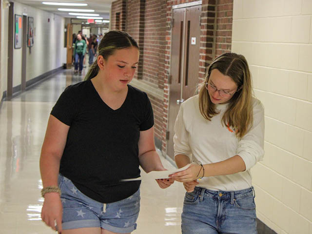 Two students referencing a paper in a hallway