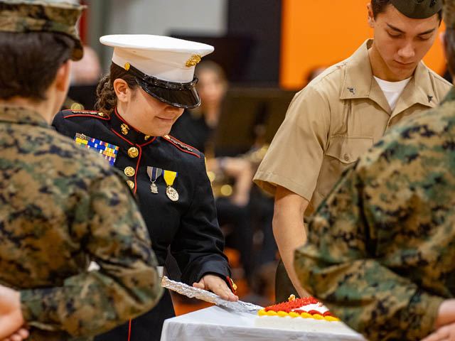 JROTC cadets stand next to the commander, who is cutting the first piece of cake at the ball