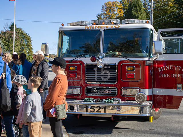A group of children and teachers gather in front of a Minetto Fire Department truck