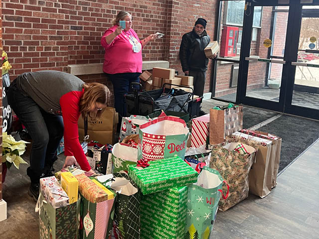 A photo of two women and a man standing in front of a large pile of wrapped Christmas presents in the lobby at Fulton Mills Apartments