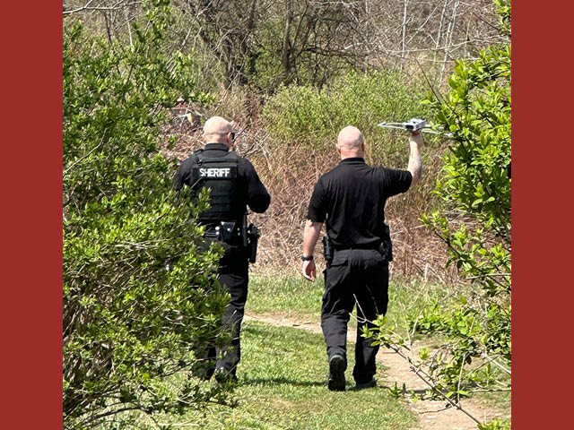 A photograph of two men from the Sheriff's office with a drone on a bushy trail