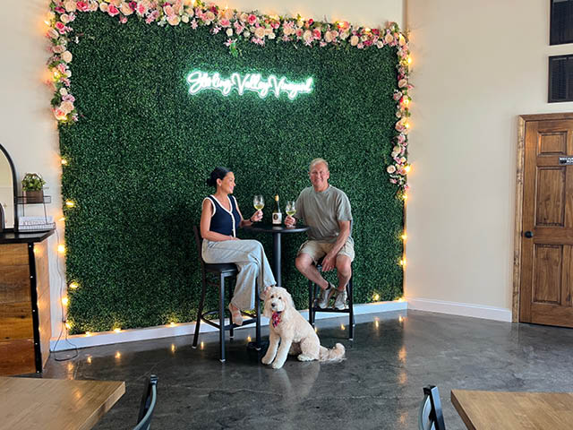 Shannon and Bill Davis sit at a table in their tasting room with service poodle Kingston at their feet