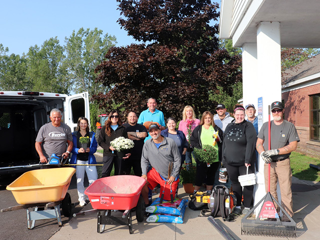 A group of volunteers and OCO employee Bridget Dolbear standing around wheelbarrows and flowers