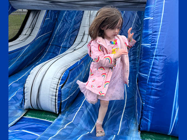 A young girl on a blue slide in a pink rain jacket