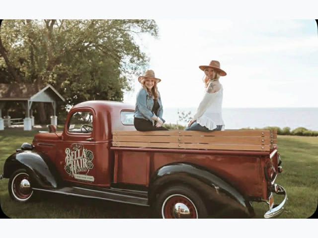 Tammy and Grace on the back of an old red pickup truck with a decal for Bella Hair Oswego on the driver's side door