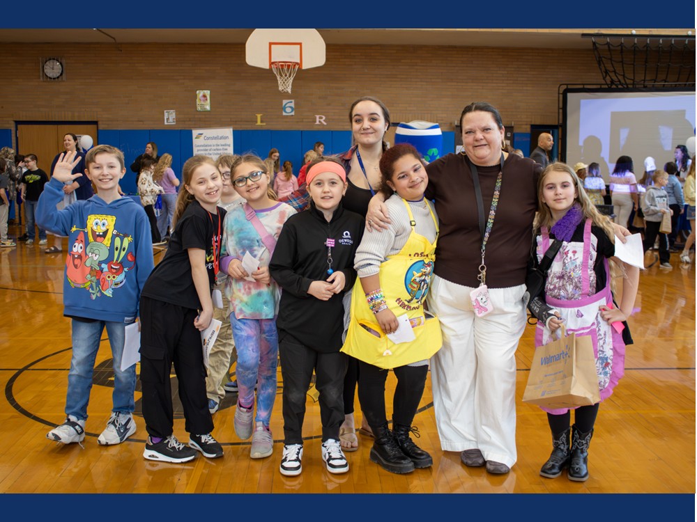 Two adults surrounded by several smiling kids in the gym.