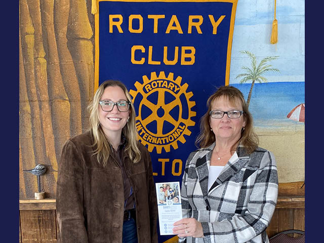 Two women stand in front of a Rotary banner