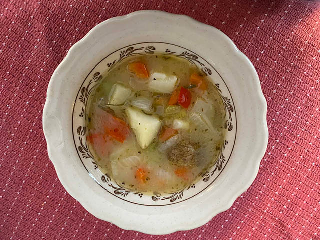 Vegetable soup in a bowl against a red tablecloth with white dotted pattern