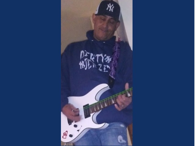 Man in blue hoodie with NY Yankees cap on playing a white electric guitar
