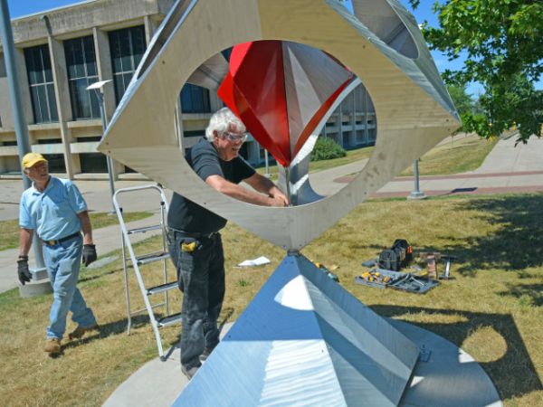 Kinetic art -- Artist Bob Turan of Earlton finishes assembling his sculpture &quot;Square Dance,&quot; the first of six sculptures installed near Marano Campus Center for the college&#039;s third biennial outdoor exhibition. The 10-foot-tall steel, stainless steel and aluminum piece features a central pinwheel that rotates even in relatively low wind. At left is Turan&#039;s assistant, Phil Restaino.
