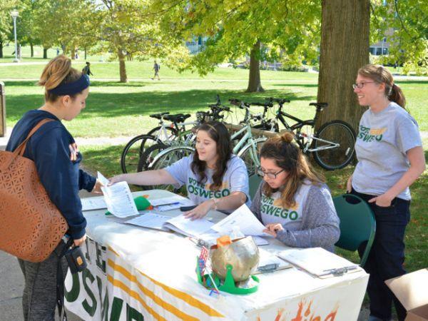 Voter drive -- SUNY Oswego senior public relations major Alexa Carrascal (right) assists senior studio art major Jennifer Varvaro (left) with a form Sept. 27 during a Vote Oswego registration event on the quad near Penfield Library. Students in political science faculty member Allison Rank&#039;s &quot;Vote Oswego&quot; course have registered hundreds of students on and off campus to vote and/or to request absentee ballots. Looking on is senior psychology major Selena Gancasz, who volunteered on behalf of her public justice class on American courts and the judicial system. Vote Oswego made coalitions with many student organizations across campus to assist with a &quot;blitz week&quot; series of registration events recently.